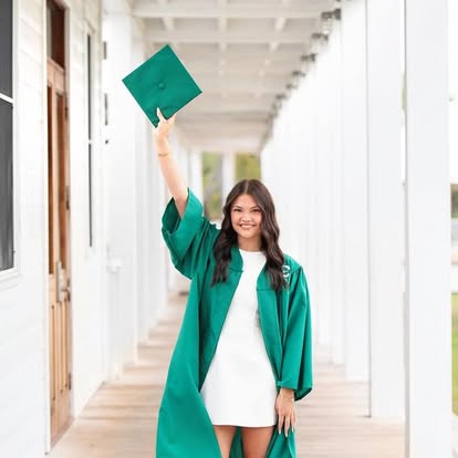 A graduate in a green cap and gown raising her cap with a bright smile